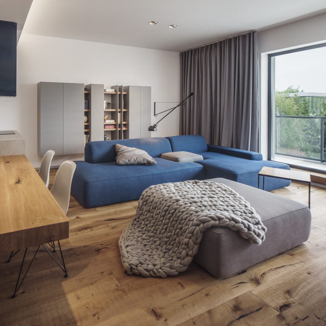 Spacious living room with blue sofa, wooden floor, and built-in shelving units.