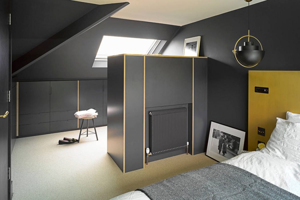 Modern attic bedroom with sleek black furniture, brass lighting, and geometric patterns.