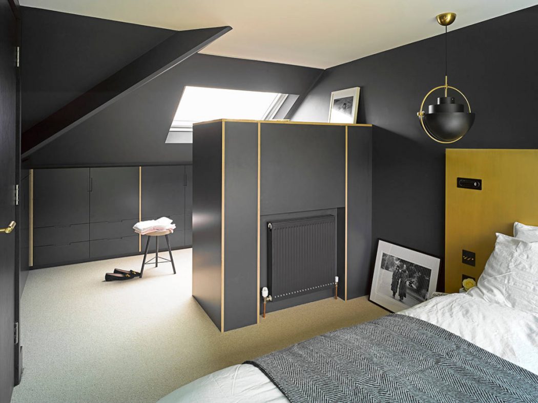 Modern attic bedroom with sleek black furniture, brass lighting, and geometric patterns.