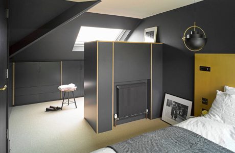 Modern attic bedroom with sleek black furniture, brass lighting, and geometric patterns.