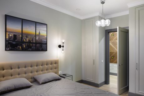 Spacious bedroom with tufted headboard, cityscape artwork, and modern lighting fixtures.