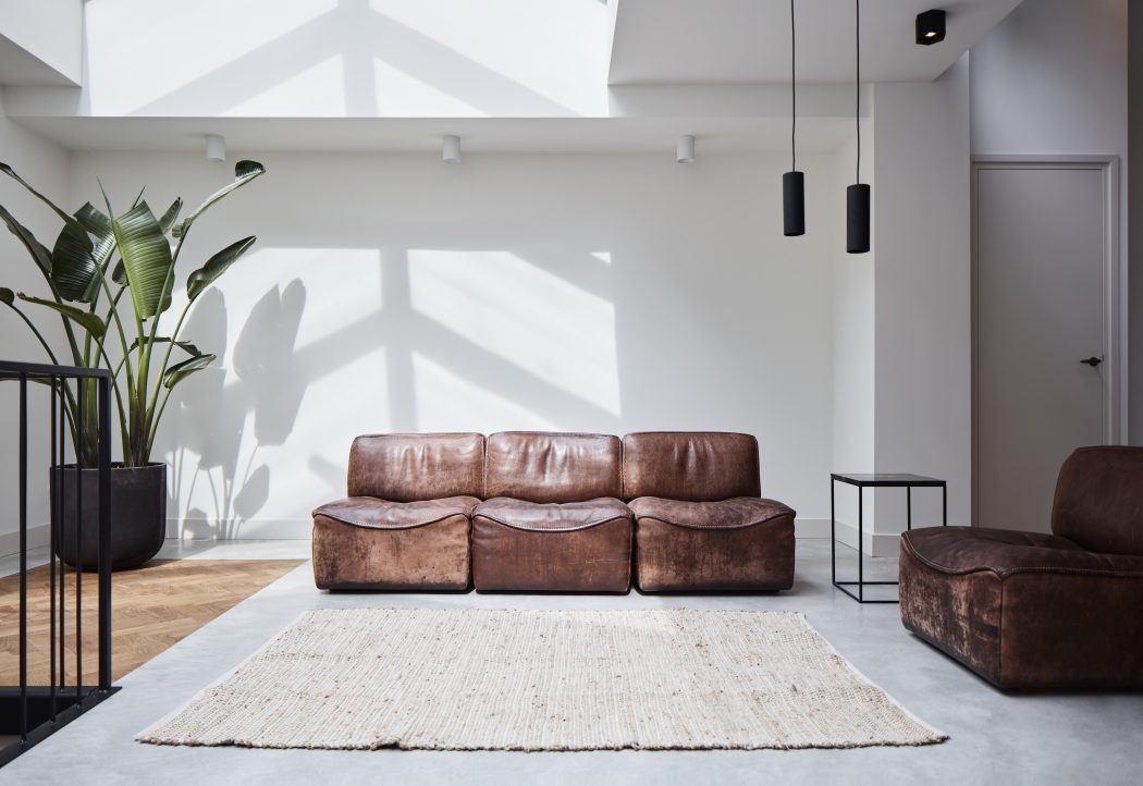 Modern living room with leather sofa, rug, and pendant lights under skylights.
