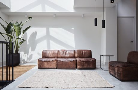 Modern living room with leather sofa, rug, and pendant lights under skylights.