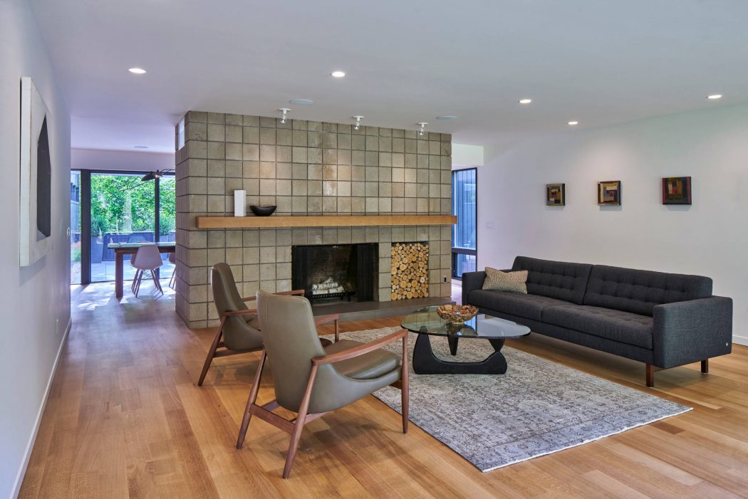 A modern, airy living room with a tiled fireplace, wooden floors, and mid-century furniture.