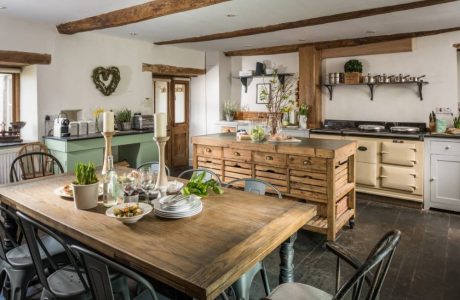 Rustic kitchen with wooden beams, island, dining table, and open shelving.