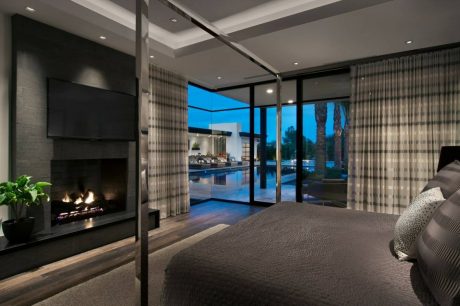 Luxurious bedroom with fireplace, floor-to-ceiling windows, and scenic pool view.