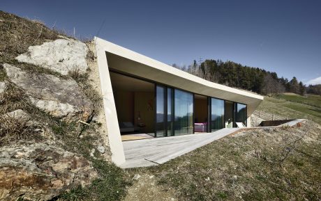 Modern home nestled into a hillside, featuring clean lines, large windows, and natural surroundings.