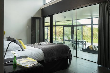 Spacious bedroom with large glass walls overlooking a lush outdoor garden.