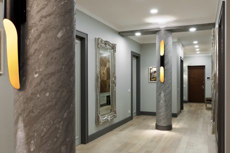 Sleek, modern hallway with marble columns, recessed lighting, and an ornate mirror.