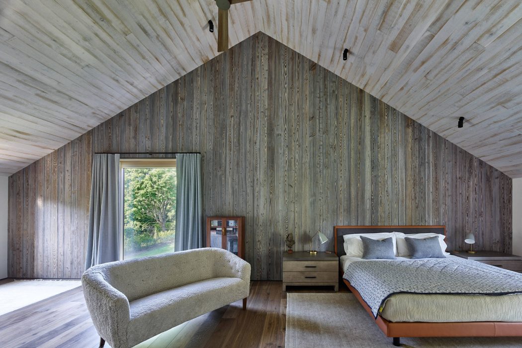 Rustic bedroom with vaulted wooden ceiling, gray plank walls, and modern furnishings.