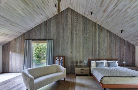 Rustic bedroom with vaulted wooden ceiling, gray plank walls, and modern furnishings.