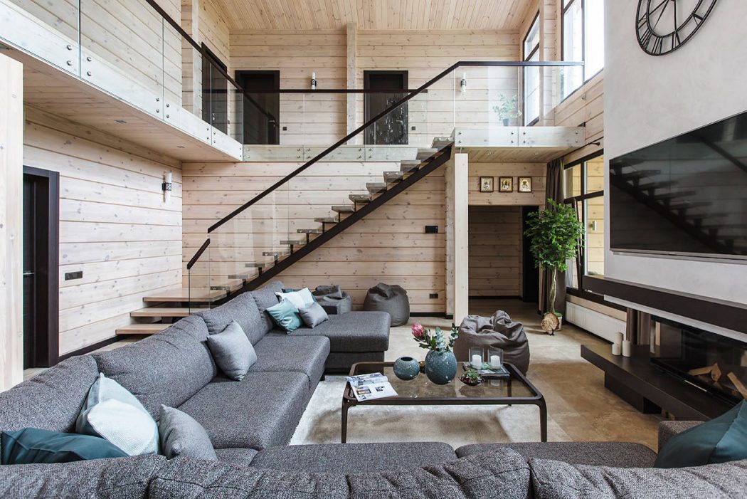 A modern, open-concept living space with wood paneling, a glass staircase, and a large sectional couch.