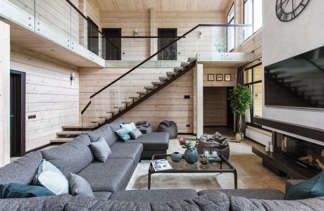 A modern, open-concept living space with wood paneling, a glass staircase, and a large sectional couch.