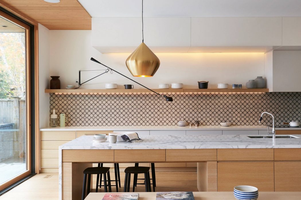 Bright, modern kitchen with wood cabinetry, marble countertops, and a statement gold pendant light.
