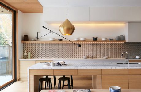 Bright, modern kitchen with wood cabinetry, marble countertops, and a statement gold pendant light.