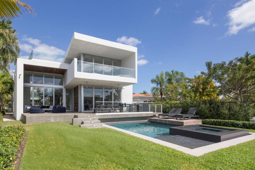 Modern, two-story house with glass walls, pool, and lush tropical landscaping.