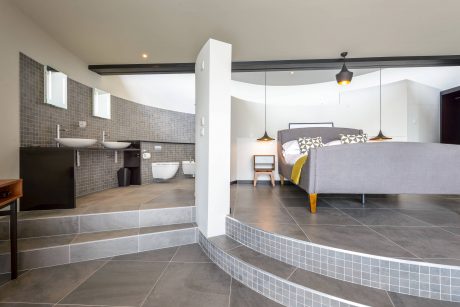 Open-concept bedroom and bathroom with sleek tile flooring, black accents, and modern lighting.