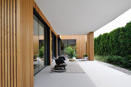 A modern, wood-paneled exterior with large glass windows, a patio, and lush greenery.