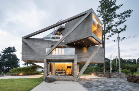 Modern concrete and glass structure with geometric angles and recessed lighting, surrounded by trees.