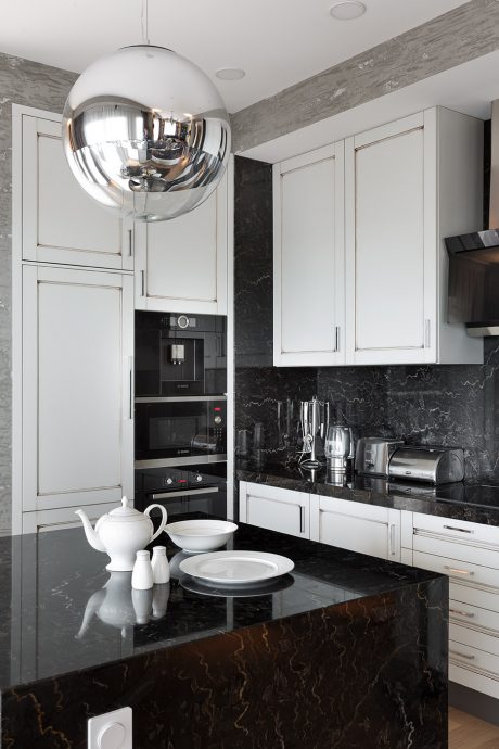 Modern kitchen with sleek white cabinetry, marble countertops, and chrome pendant light.