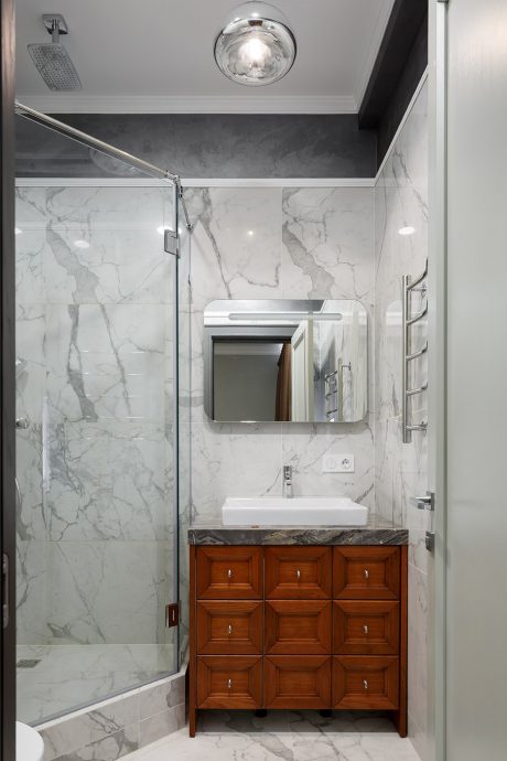 A modern bathroom with marble walls, glass shower, and elegant wooden vanity cabinet.