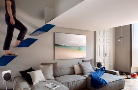 A modern living room with intricate wooden flooring, a gray sectional sofa, and geometric artwork on the wall.