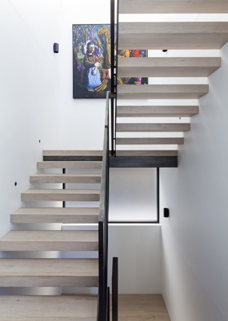 Sleek, minimalist staircase with floating wood treads against a backdrop of artworks.