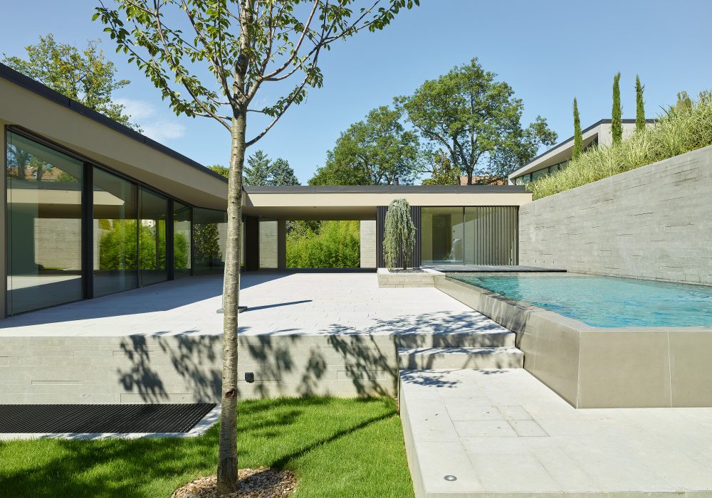 Modernist home with glass walls, swimming pool, and lush landscaping. Sleek, minimalist design.