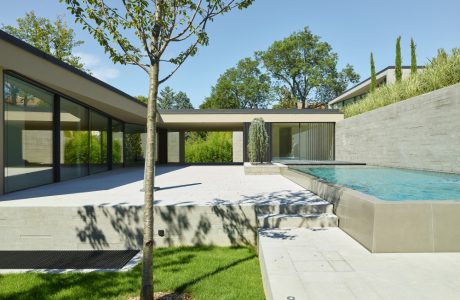 Modernist home with glass walls, swimming pool, and lush landscaping. Sleek, minimalist design.