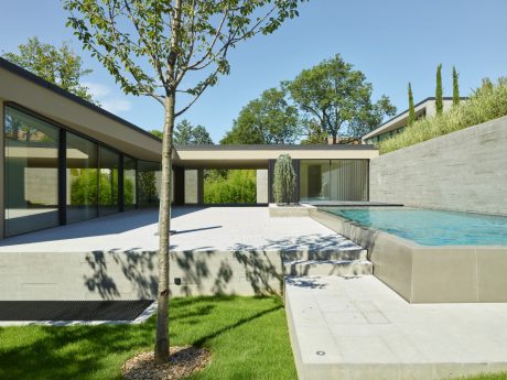 Modernist home with glass walls, swimming pool, and lush landscaping. Sleek, minimalist design.