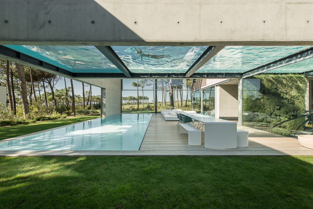 Glass-enclosed pool area with modern, minimalist furniture and lush greenery surrounding it.