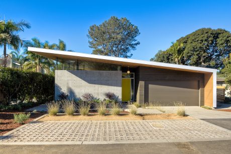 A modern, single-story home with a flat roof, wood and concrete exterior, and a prominent garage door.
