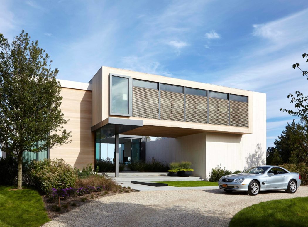 Modern, sophisticated architecture with sleek design and glass features. Landscaped garden and luxury car in driveway.