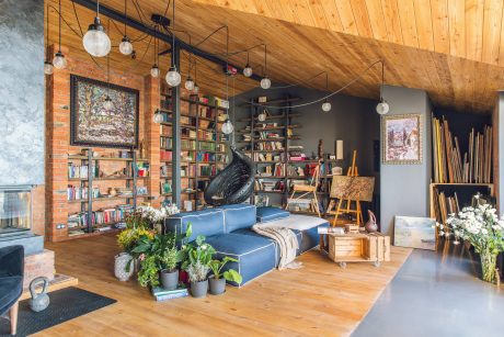 A cozy living space with wooden walls, shelves, and hanging globe lights, complemented by a blue couch and artwork.