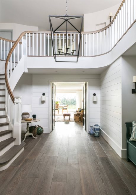 Spacious foyer with rustic wood floors, curved staircase, and modern chandelier.