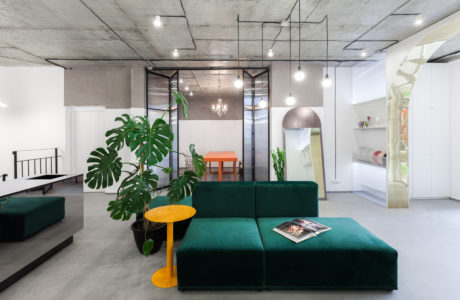 Industrial-style living space with concrete ceiling, lush greenery, and vibrant furniture.