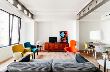 Colorful, retro-inspired living space with wooden furniture, contemporary artwork, and varied seating.