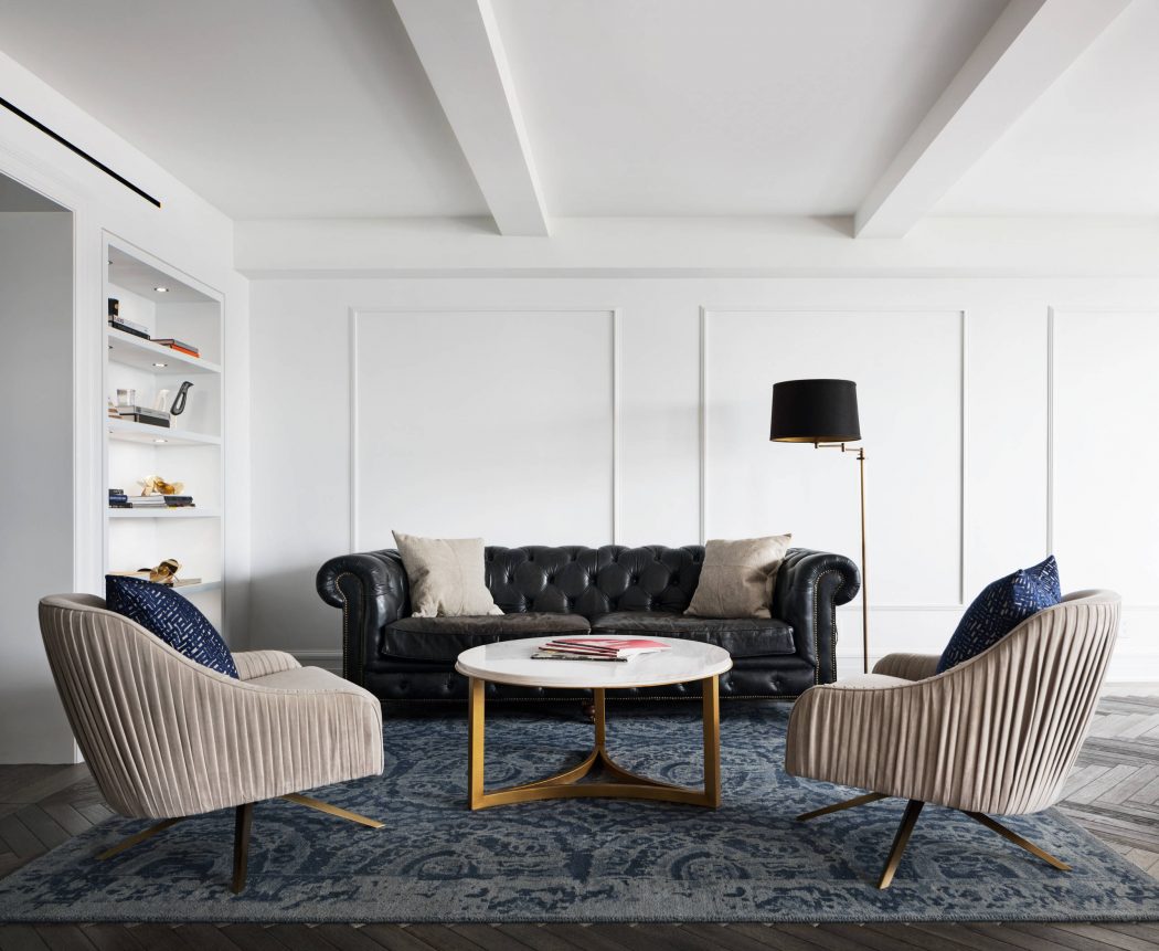 Sleek, minimalist living room with tufted leather sofa, plush armchairs, and a modern coffee table on a patterned rug.