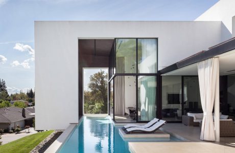 Sleek, modern home with a long, narrow pool, surrounded by lush greenery and clear skies.