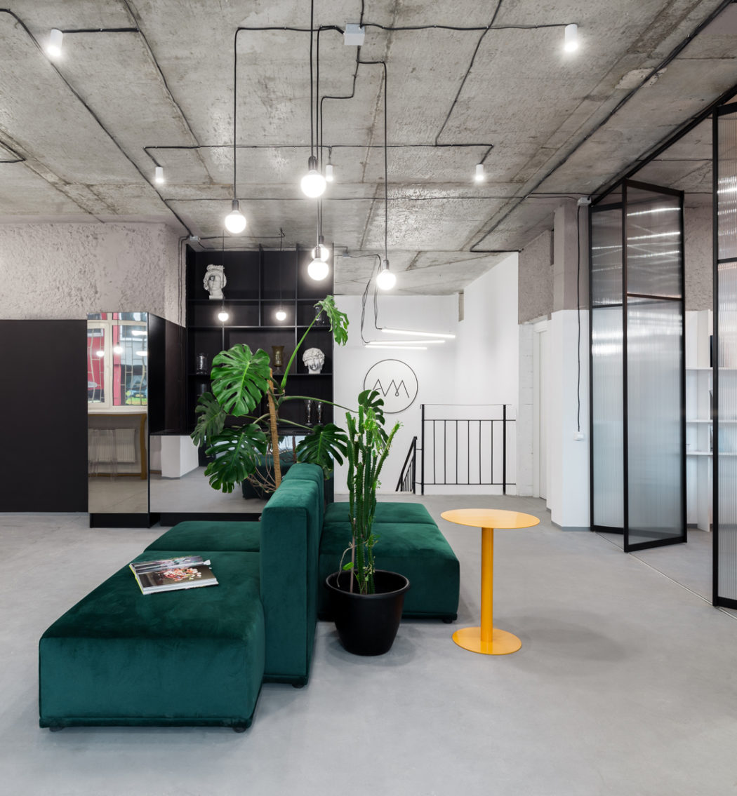 A modern, industrial-style office design with a plush green sofa, potted plants, and sleek lighting fixtures.