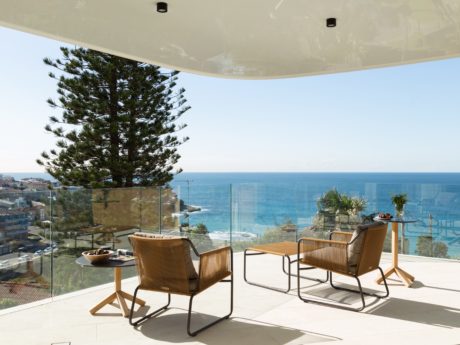 Outdoor patio with glass walls and panoramic ocean view, minimalist furniture and decor.