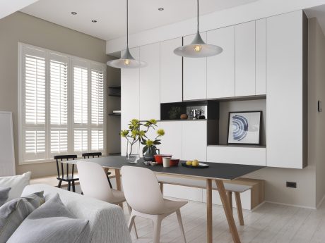 A modern, minimalist dining room with white cabinets, black worktop, and pendant lights.