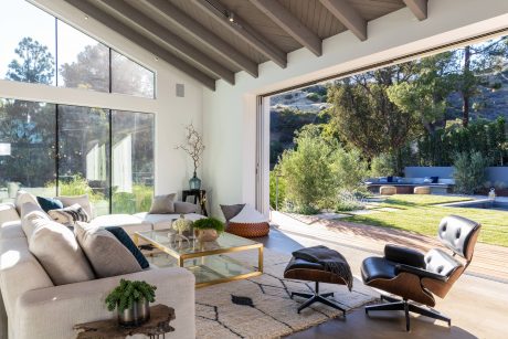 Expansive, modern living room with panoramic glass walls, wooden beams, and plush furnishings.