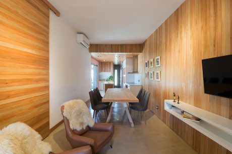 A modern, cozy living room with wooden walls, a dining table, and comfortable seating.