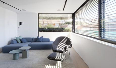 Minimalist living room with modular seating, striped chair, and large windows overlooking greenery.