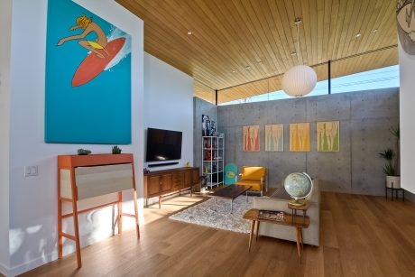 Bright, mid-century modern room with wood paneling, concrete walls, and colorful artwork.