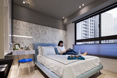 Sleek, modern bedroom with marble accent wall, large windows, and a person relaxing on the bed.