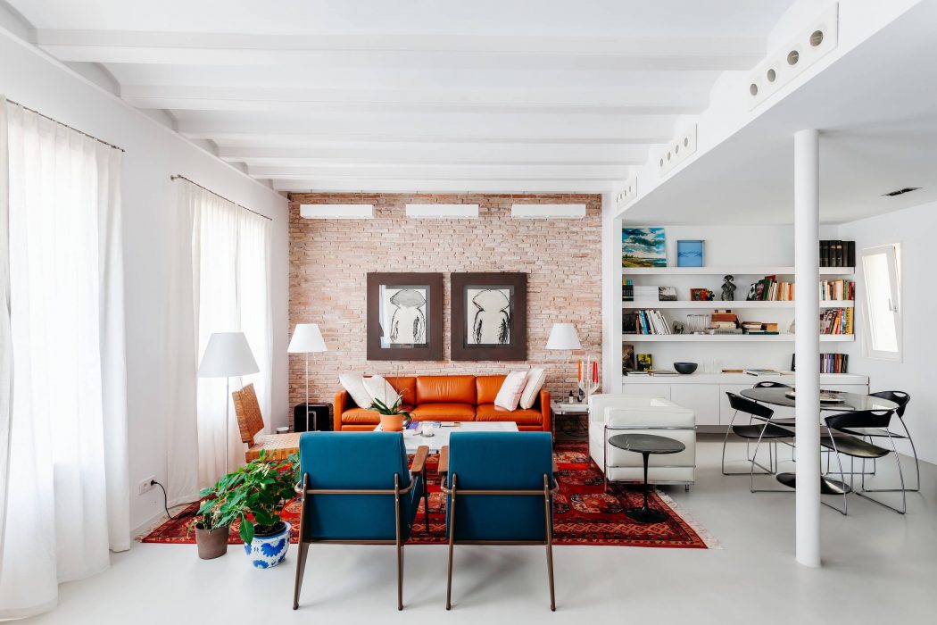 Bright, airy living room with exposed brick walls, vibrant orange sofa, and modern shelving.