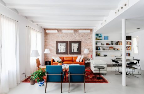 Bright, airy living room with exposed brick walls, vibrant orange sofa, and modern shelving.