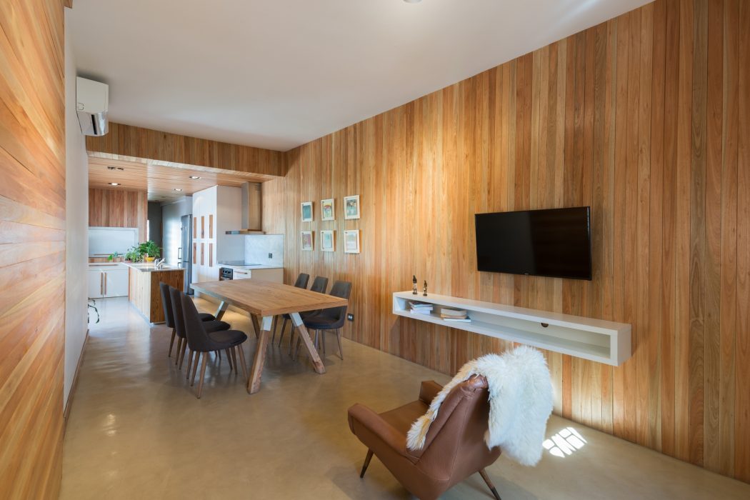 Modern open-plan living space with warm wooden walls, comfortable furnishings, and sleek media setup.